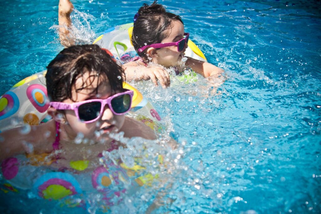 Two young girls swimming in a pool with goggles on.