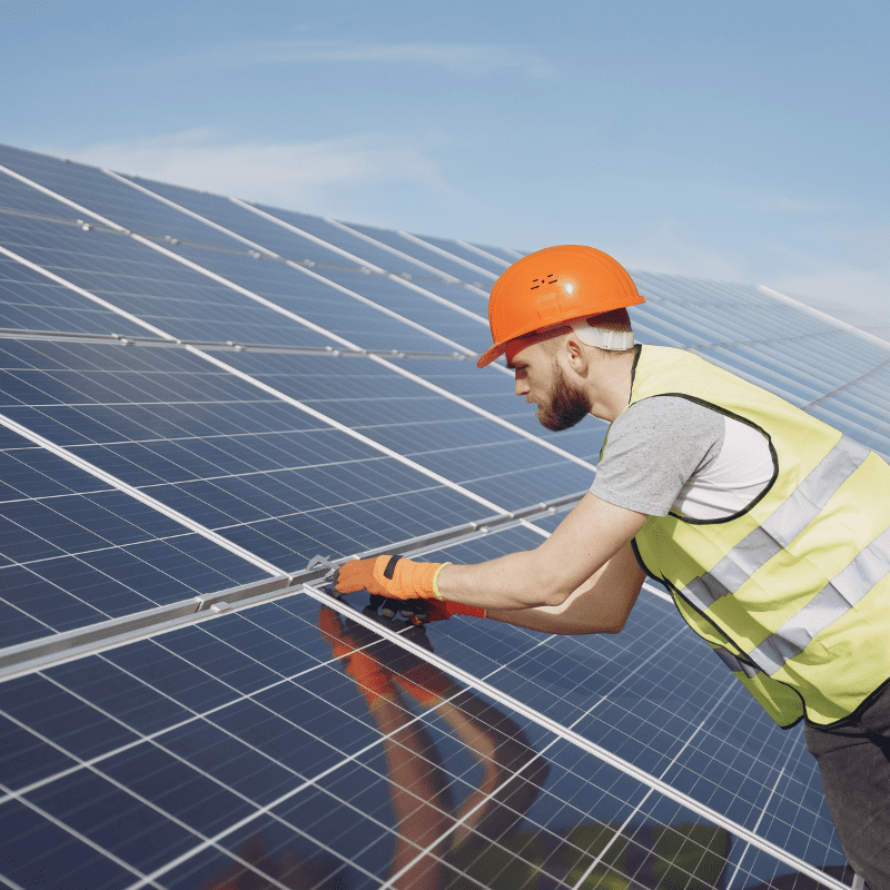 A man in an orange hard hat and safety vest working on solar panels.