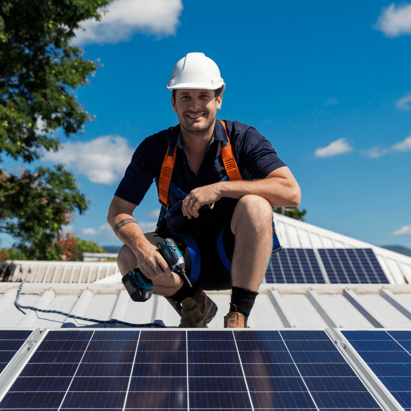 A man kneeling down on the roof of a house.