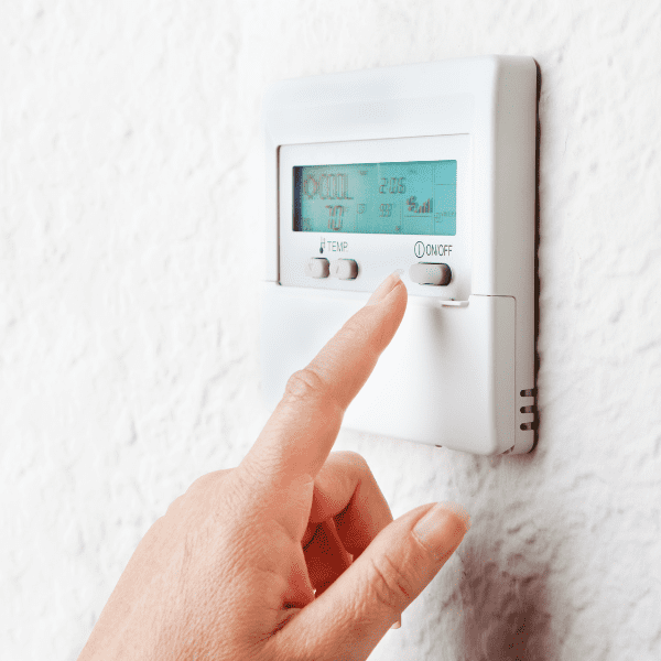 A person is pointing to the thermostat on their wall.