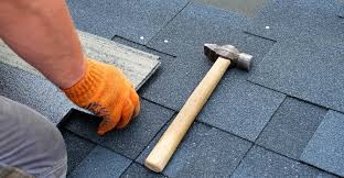 A man laying roof tiles wearing gloves and with a hammer